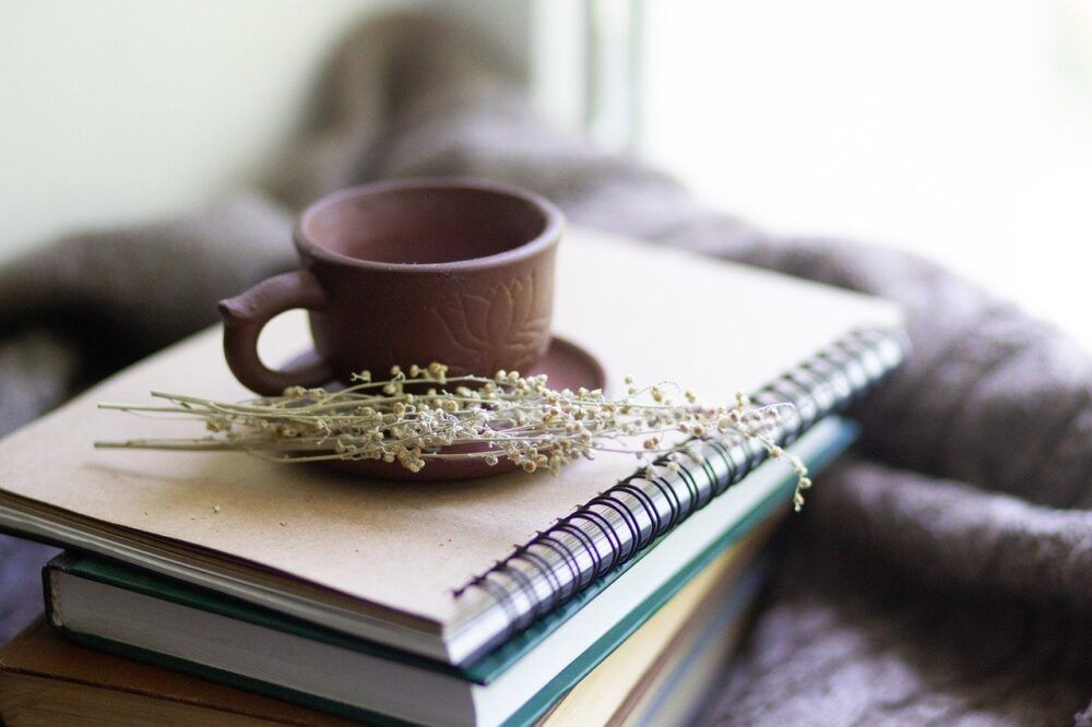 Foto von einer Tasse Tee die auf einem Stapel Büchern und Heften liegt, daneben liegt ein BundKräuter